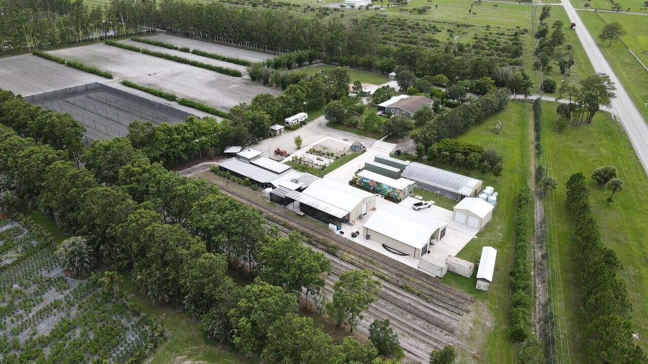 An aerial view shows a rural property with multiple buildings, greenhouses, and agricultural fields — 8006 SW Kanner Highway, FL 34956, FL