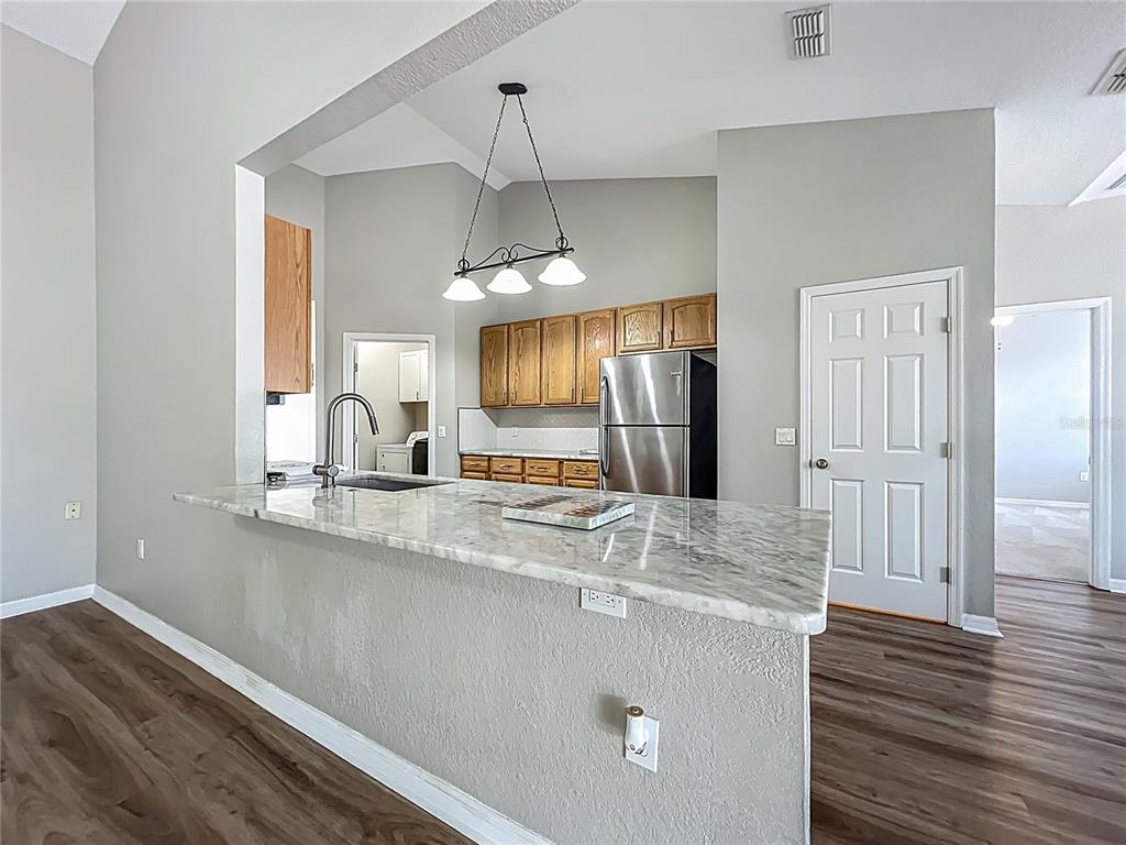A kitchen with a marble-topped breakfast bar, stainless steel refrigerator, and wood cabinets — 301 TERRANOVA BOULEVARD, WINTER HAVEN, FL