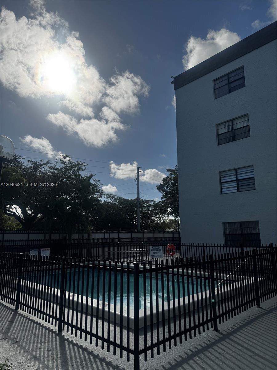 A fenced-in swimming pool sits beside a multi-story apartment building under a sunny sky — 13500 NE 3rd Ct # 120, North Miami FL 33161, NORTH MIAMI, FL