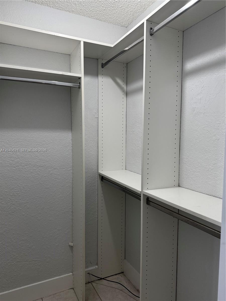 A walk-in closet features white shelving units with hanging rods and a tiled floor — 13500 NE 3rd Ct # 120, North Miami FL 33161, NORTH MIAMI, FL