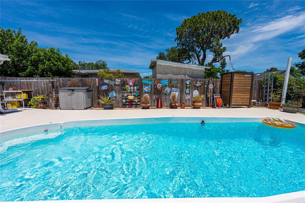 A backyard swimming pool features a wooden fence decorated with vintage signs and potted plants — 5760 3RD AVENUE N, ST PETERSBURG, FL