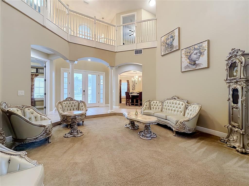 A formal living room features a two-story ceiling, carpeted floors, and ornate cream-colored furniture — 3405 HEIRLOOM ROSE PLACE, OVIEDO, FL
