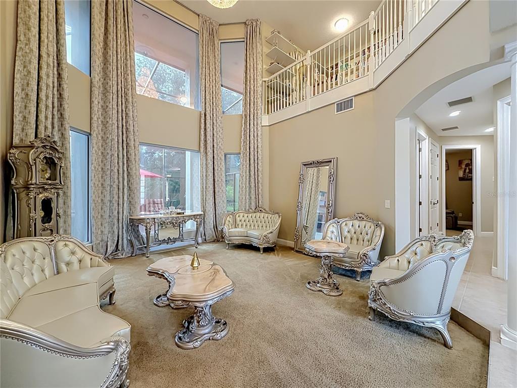 A formal living room features high ceilings, floor-to-ceiling curtains, and ornate, light-colored furniture — 3405 HEIRLOOM ROSE PLACE, OVIEDO, FL