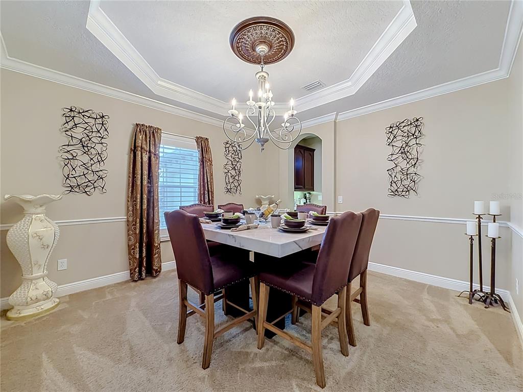 A dining room features a square marble table, upholstered chairs, a chandelier, and beige walls — 3405 HEIRLOOM ROSE PLACE, OVIEDO, FL