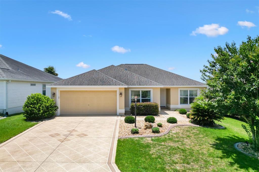 A single-story house with a tan exterior, a two-car garage, and a paved driveway — 3104 BLACKSTOCK WAY, THE VILLAGES, FL