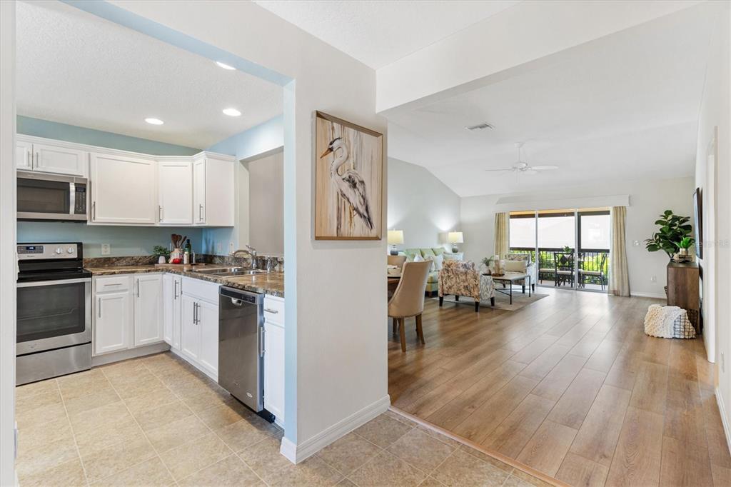 A kitchen with white cabinets and tile floors opens into a living area with wood flooring — 3104 BLACKSTOCK WAY, THE VILLAGES, FL