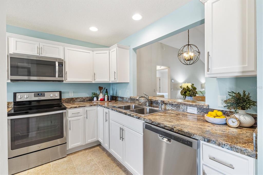 A kitchen features white cabinets, granite countertops, stainless steel appliances, and a pass-through window — 3104 BLACKSTOCK WAY, THE VILLAGES, FL