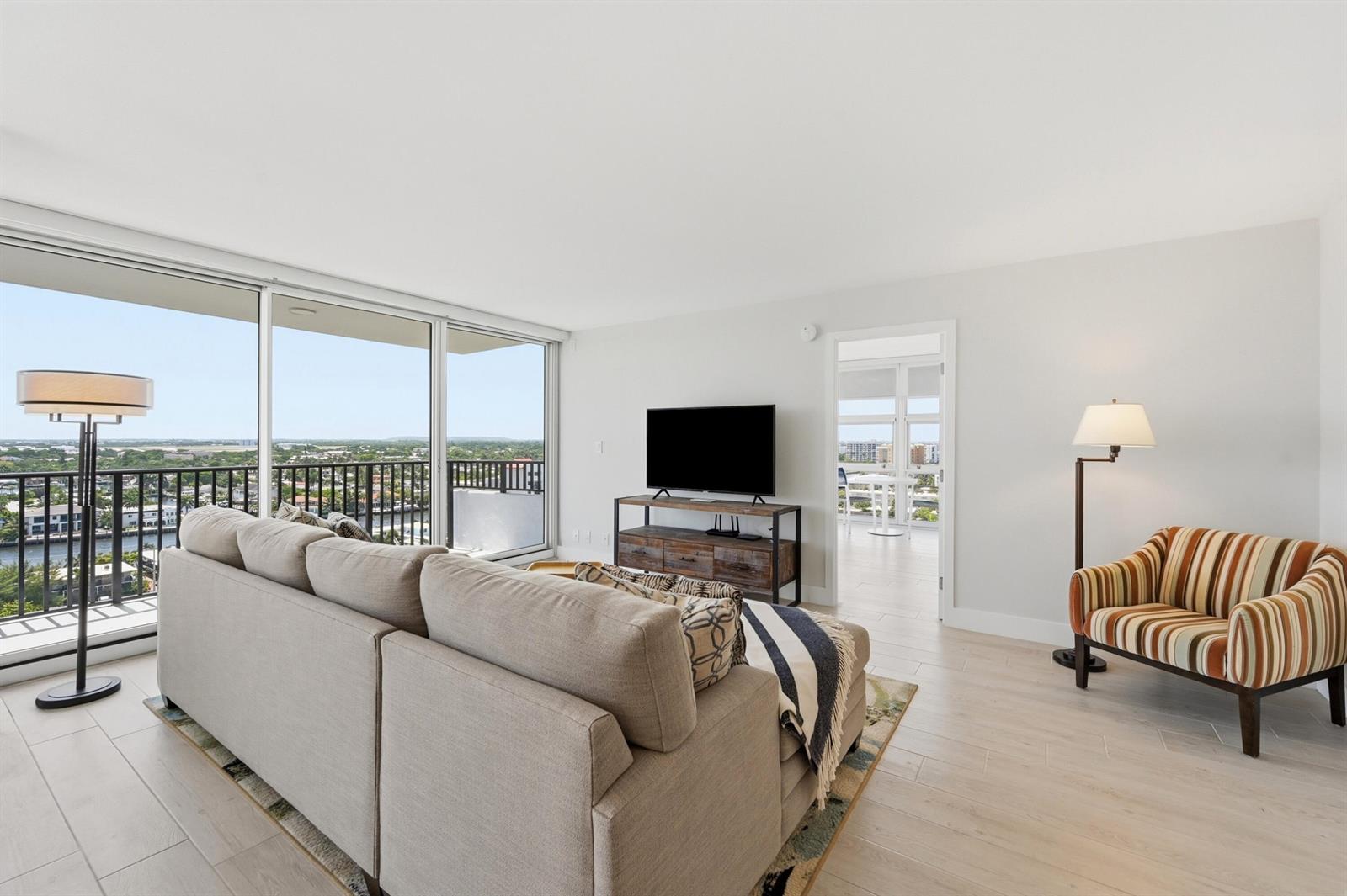 A living room features a sectional sofa, striped armchair, television console, and floor-to-ceiling windows — 531 N Ocean Boulevard # 1601, Pompano Beach FL 33062, POMPANO BEACH, FL