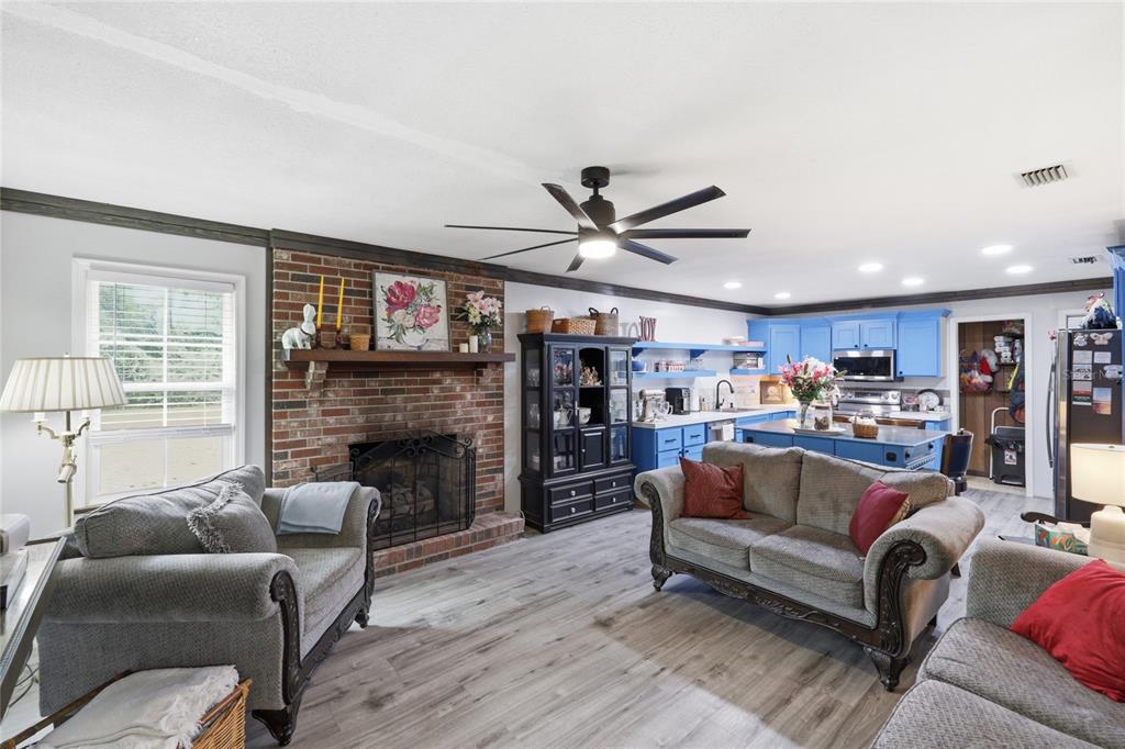 A living room features a brick fireplace, grey wood-look flooring, and an open blue kitchen — 1638 SW KING STREET, LAKE CITY, FL