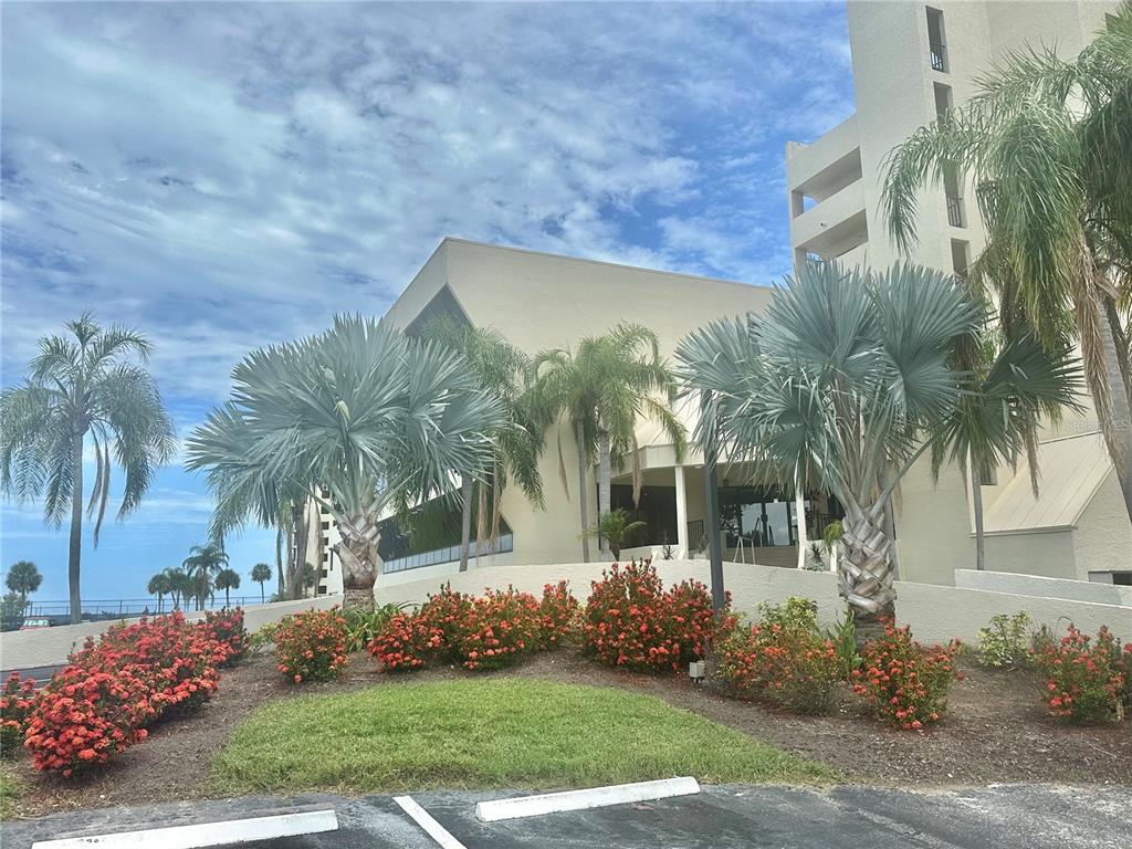 A multi-story building exterior features palm trees and red flowering shrubs in the foreground — 6009 SEA RANCH DRIVE UNIT 707, HUDSON, FL