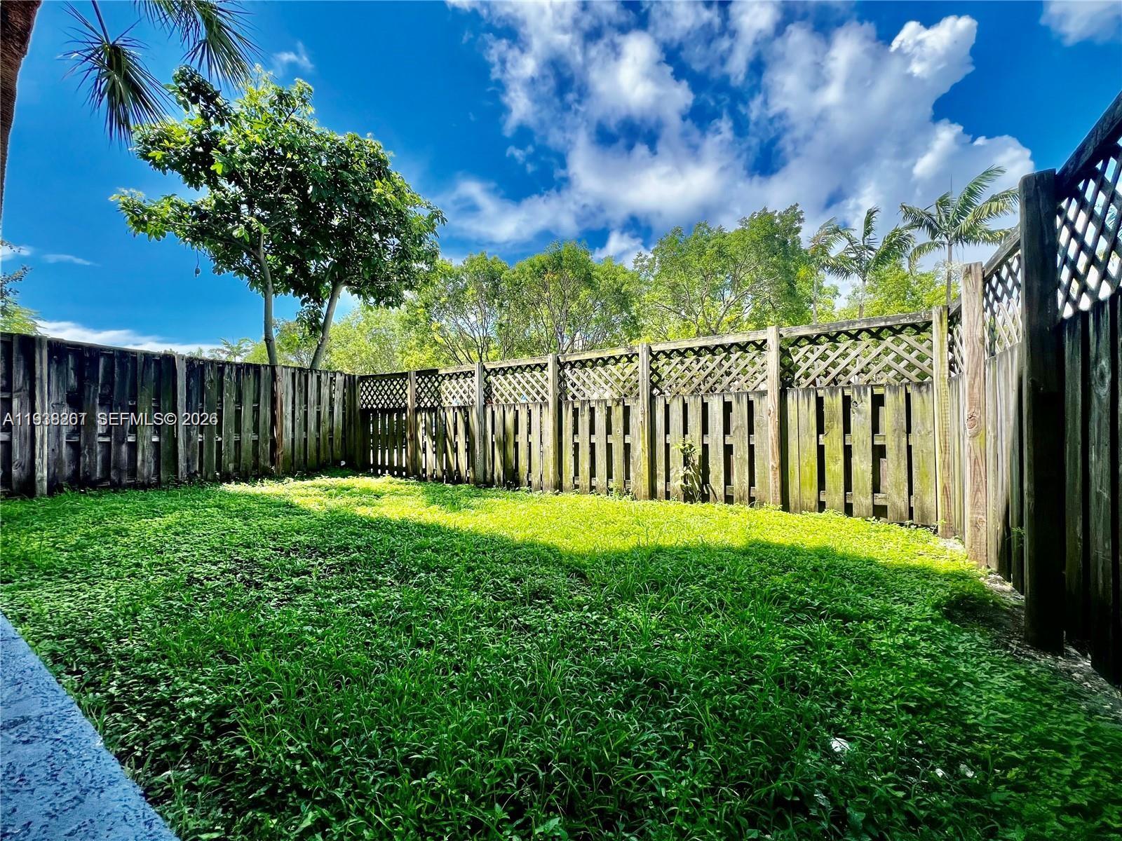 A grassy backyard is enclosed by a tall wooden fence with lattice detailing — 5201 Geneva Way # 109, Doral FL 33166, DORAL, FL