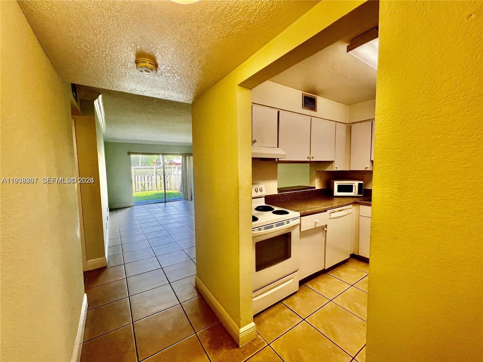A kitchen with white appliances and cabinets opens into a tiled living area with sliding doors — 5201 Geneva Way # 109, Doral FL 33166, DORAL, FL
