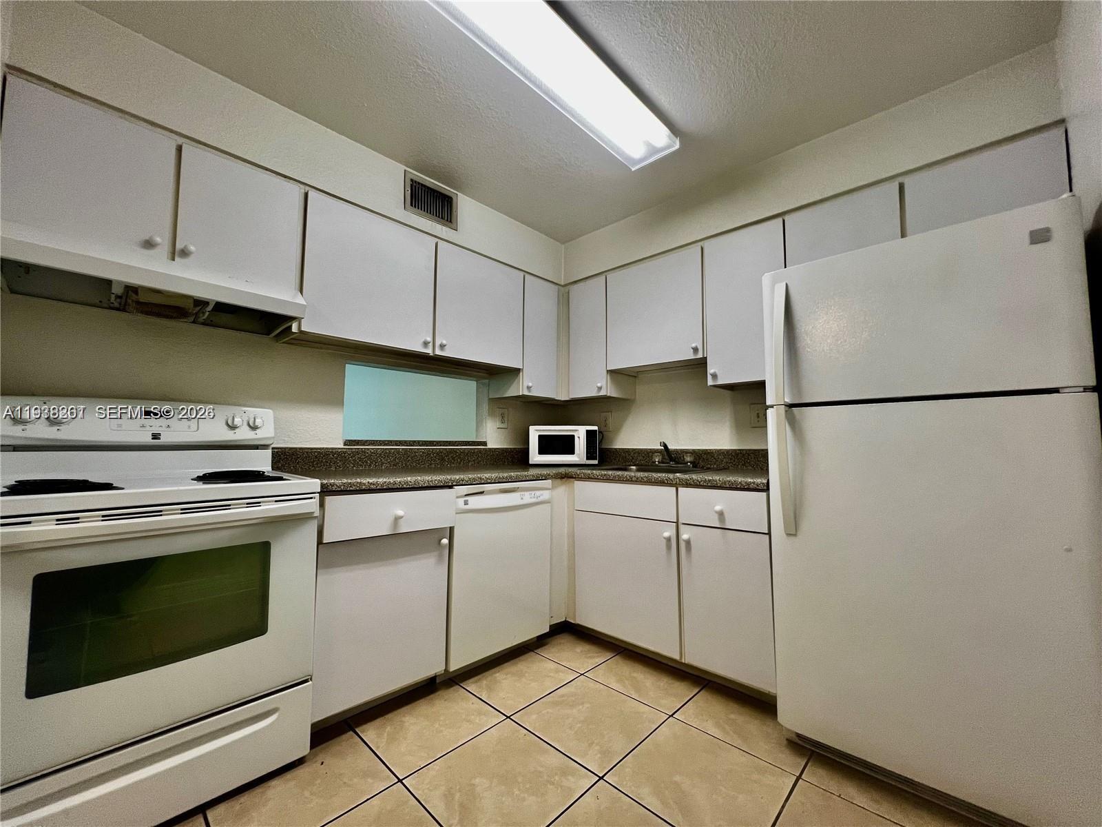 A kitchen features white cabinets, white appliances, a speckled countertop, and light-colored tile flooring — 5201 Geneva Way # 109, Doral FL 33166, DORAL, FL