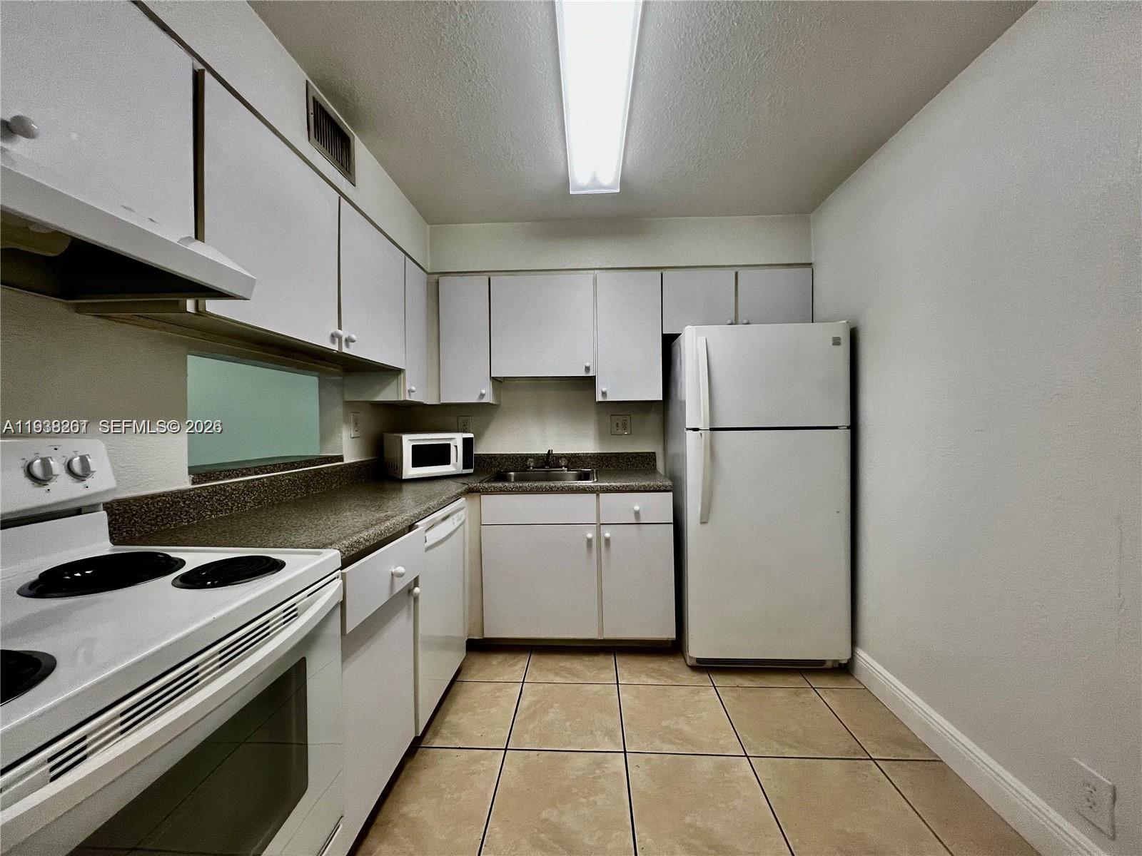 A galley kitchen features white cabinets, white appliances, a speckled countertop, and tiled flooring — 5201 Geneva Way # 109, Doral FL 33166, DORAL, FL