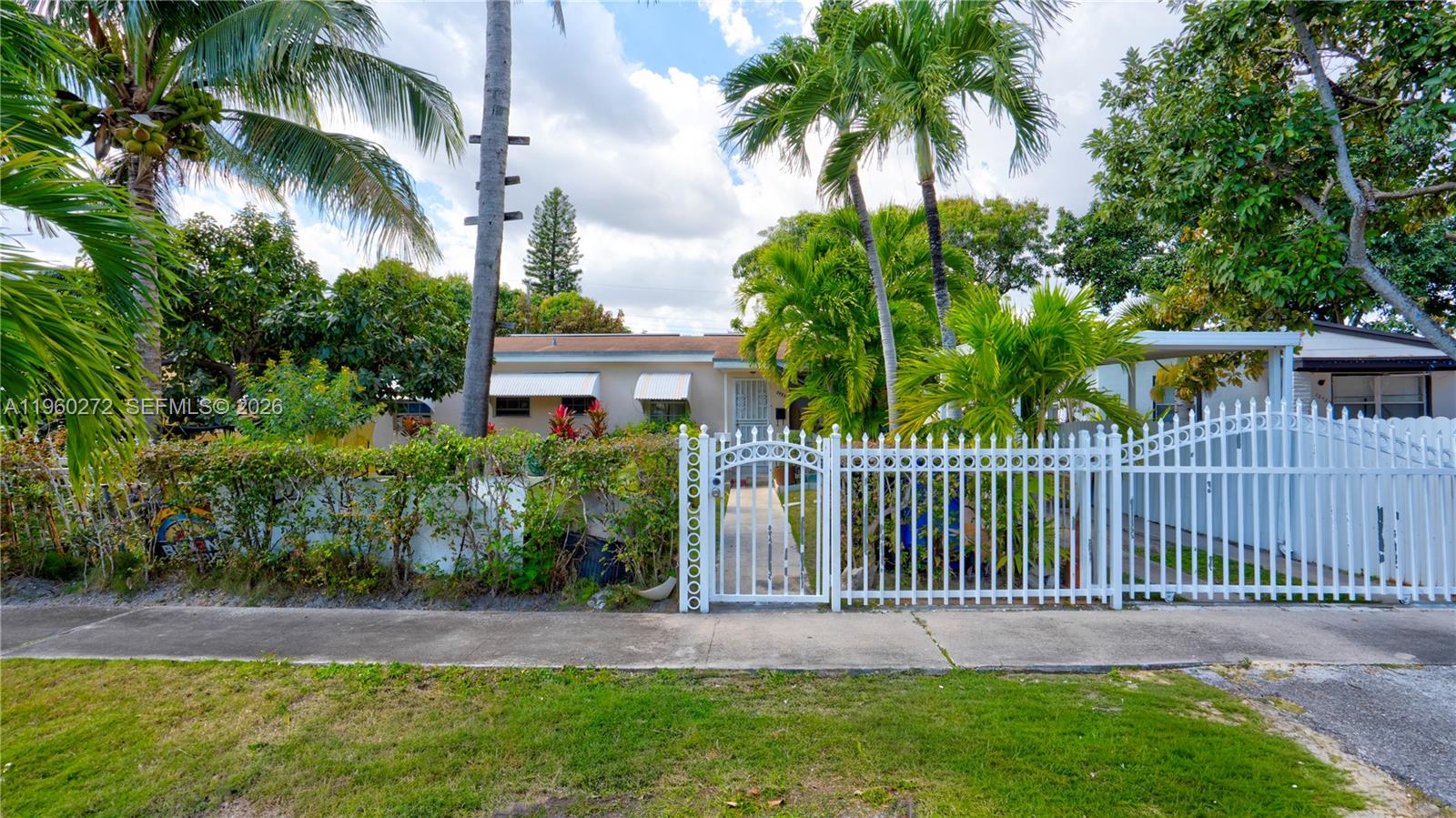 A single-story house with a white fence and gate sits behind a lush front yard — 15700 NE 15th Pl, North Miami Beach FL 33162, NORTH MIAMI BEACH, FL
