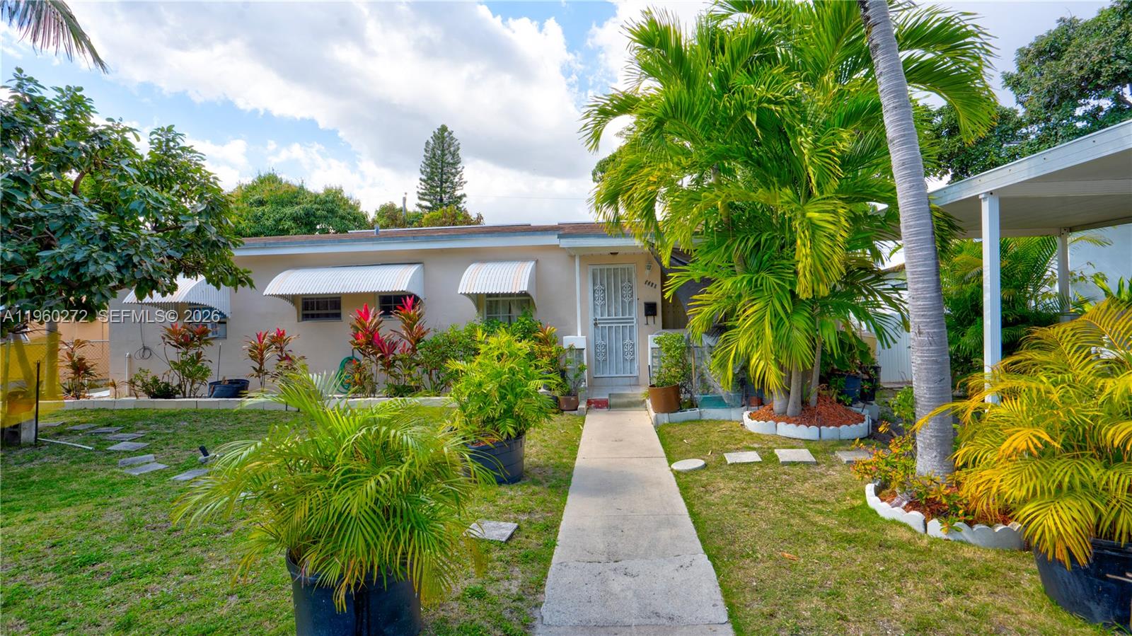 A single-story house with a concrete walkway, metal awnings, and lush tropical landscaping — 15700 NE 15th Pl, North Miami Beach FL 33162, NORTH MIAMI BEACH, FL