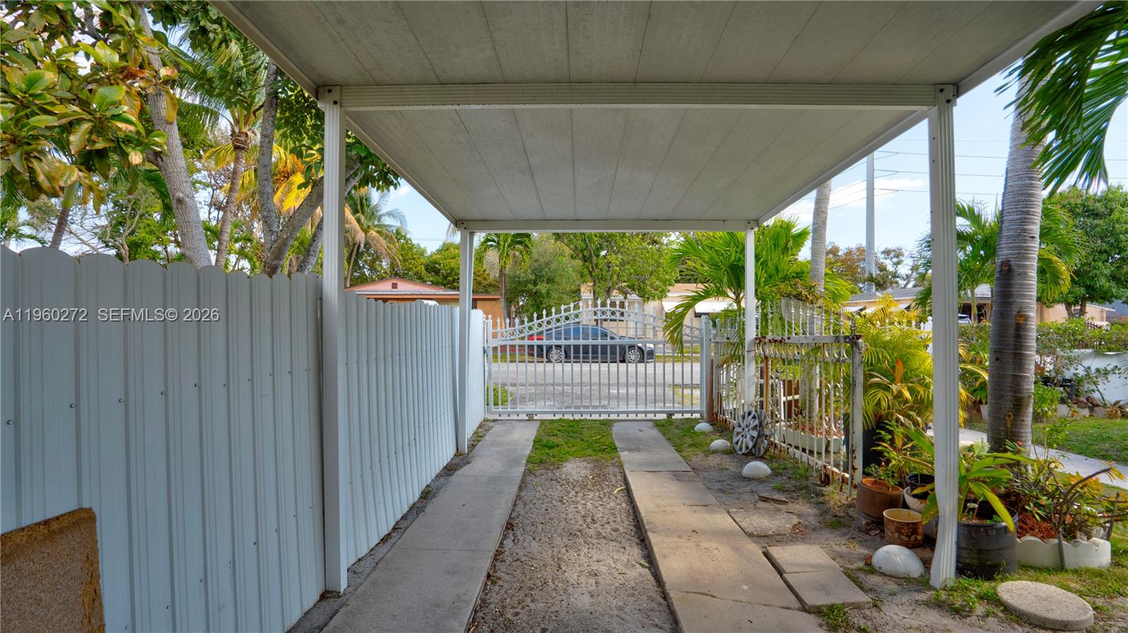 A covered carport features a concrete driveway leading to a metal gate and fence — 15700 NE 15th Pl, North Miami Beach FL 33162, NORTH MIAMI BEACH, FL