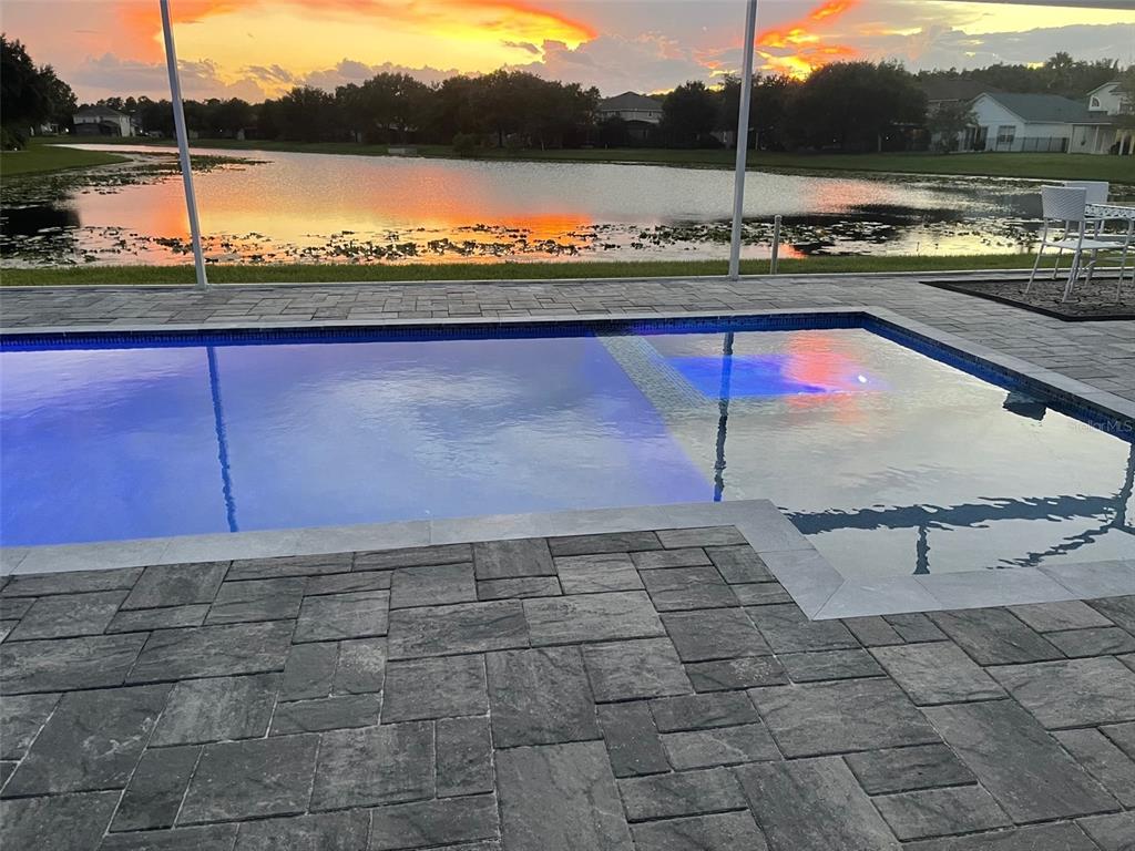 A swimming pool with a sun shelf overlooks a lake at sunset — 5338 LOS PALMA VISTA DRIVE, ORLANDO, FL