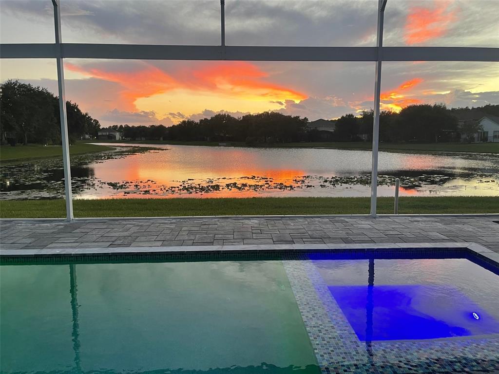 A swimming pool with a spa overlooks a lake at sunset from a screened patio — 5338 LOS PALMA VISTA DRIVE, ORLANDO, FL