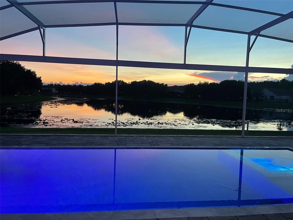 A swimming pool with a screen enclosure overlooks a lake at sunset — 5338 LOS PALMA VISTA DRIVE, ORLANDO, FL