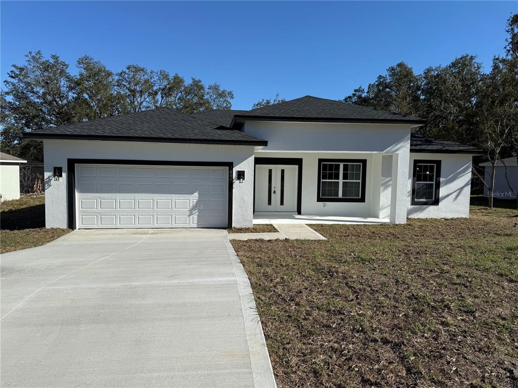 A white single-story house with a black roof, dark trim, and a concrete driveway — 7897 N FIELDSTONE DRIVE, CITRUS SPRINGS, FL
