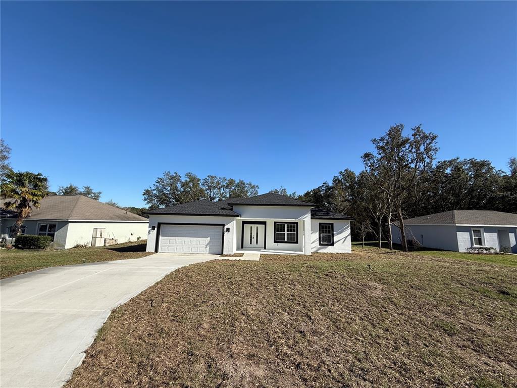 A single-story white house with a dark roof and a concrete driveway under a clear sky — 7897 N FIELDSTONE DRIVE, CITRUS SPRINGS, FL