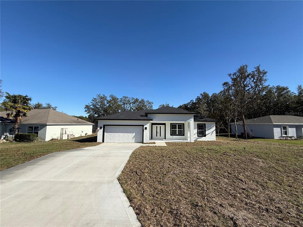 A single-story white house with a dark roof and a concrete driveway sits on grass — 7897 N FIELDSTONE DRIVE, CITRUS SPRINGS, FL