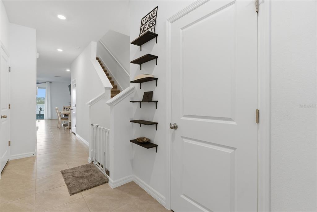 A hallway features tile flooring, a staircase with a baby gate, and wall-mounted floating shelves — 444 MANGROVE SHADE CIRCLE, APOLLO BEACH, FL