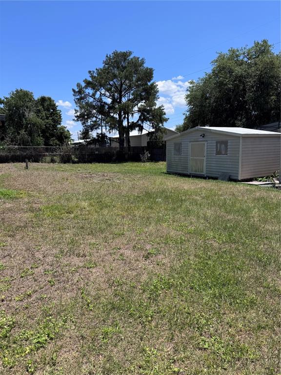 A grassy backyard features a small storage shed and a large tree under a blue sky — 4764 MALLARD DRIVE, ST CLOUD, FL