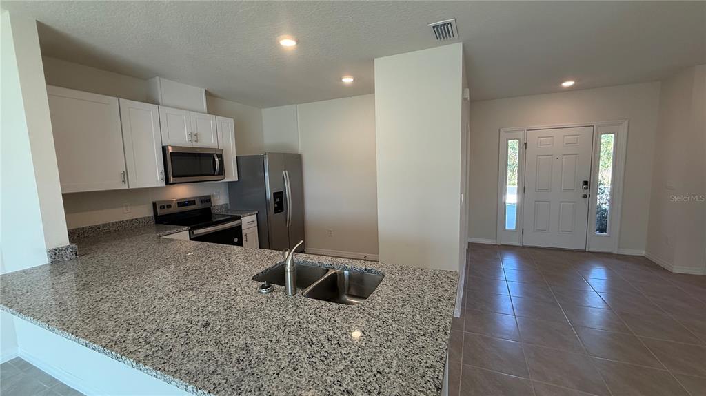 A kitchen with granite countertops and stainless steel appliances overlooks an entryway with tiled floors — 2114 GENTLE RAIN DRIVE, EDGEWATER, FL