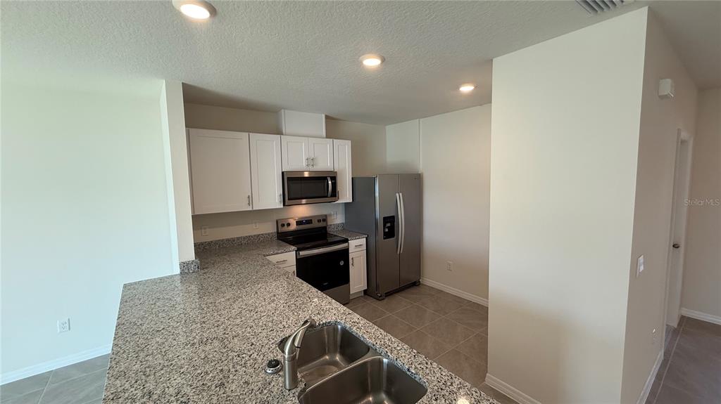 A kitchen features granite countertops, white cabinets, stainless steel appliances, and tile flooring — 2114 GENTLE RAIN DRIVE, EDGEWATER, FL