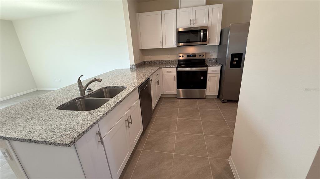 A kitchen with white cabinets, granite countertops, stainless steel appliances, and tile flooring — 2114 GENTLE RAIN DRIVE, EDGEWATER, FL