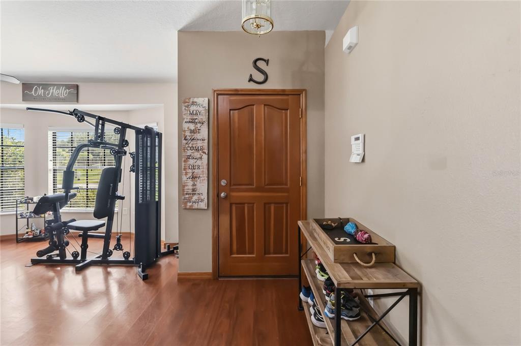 An entryway features wood flooring, a wooden front door, a home gym, and a shoe rack — 2207 DEATA COURT, ST CLOUD, FL