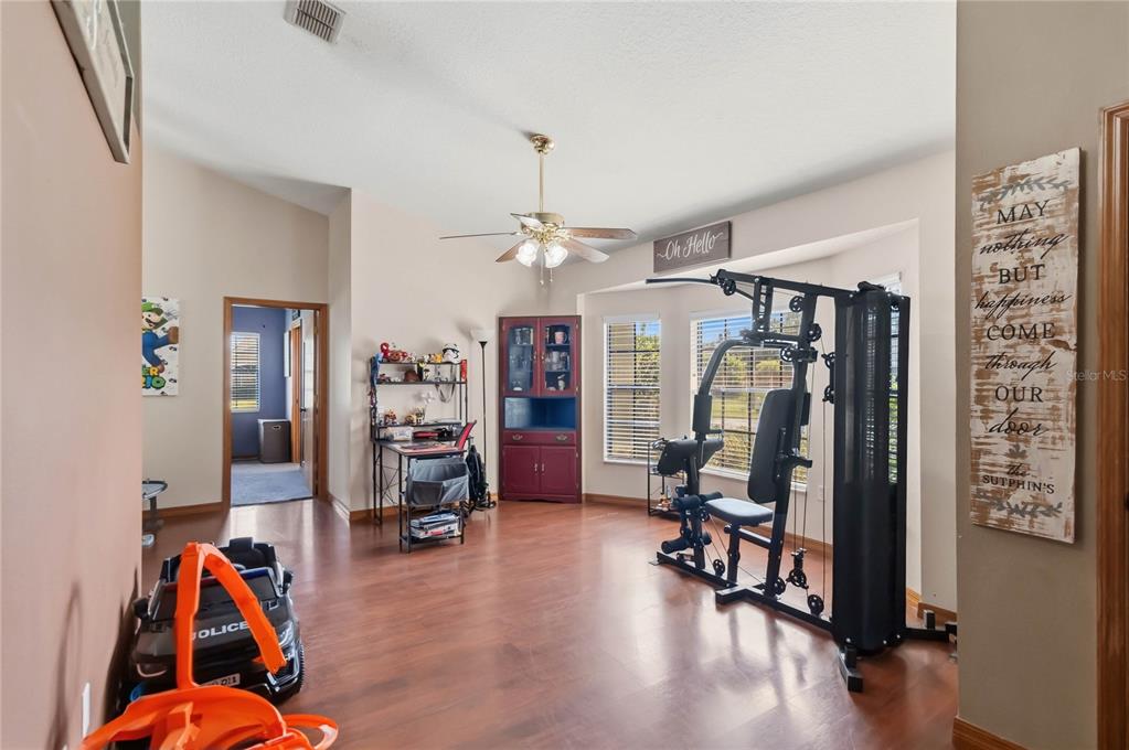 A room with wood-look flooring, a ceiling fan, a home gym machine, and a desk — 2207 DEATA COURT, ST CLOUD, FL