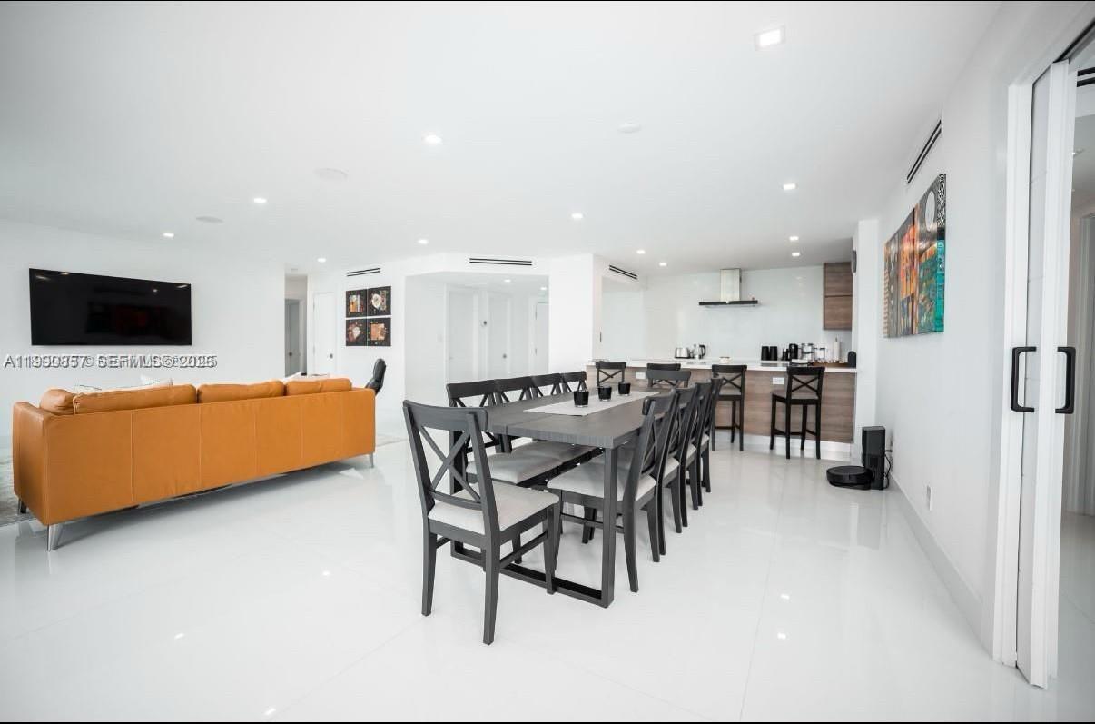 An open-concept living and dining area features white tile floors, a tan sofa, and kitchen — 5600 Collins Ave # 14K, Miami Beach FL 33140, MIAMI BEACH, FL
