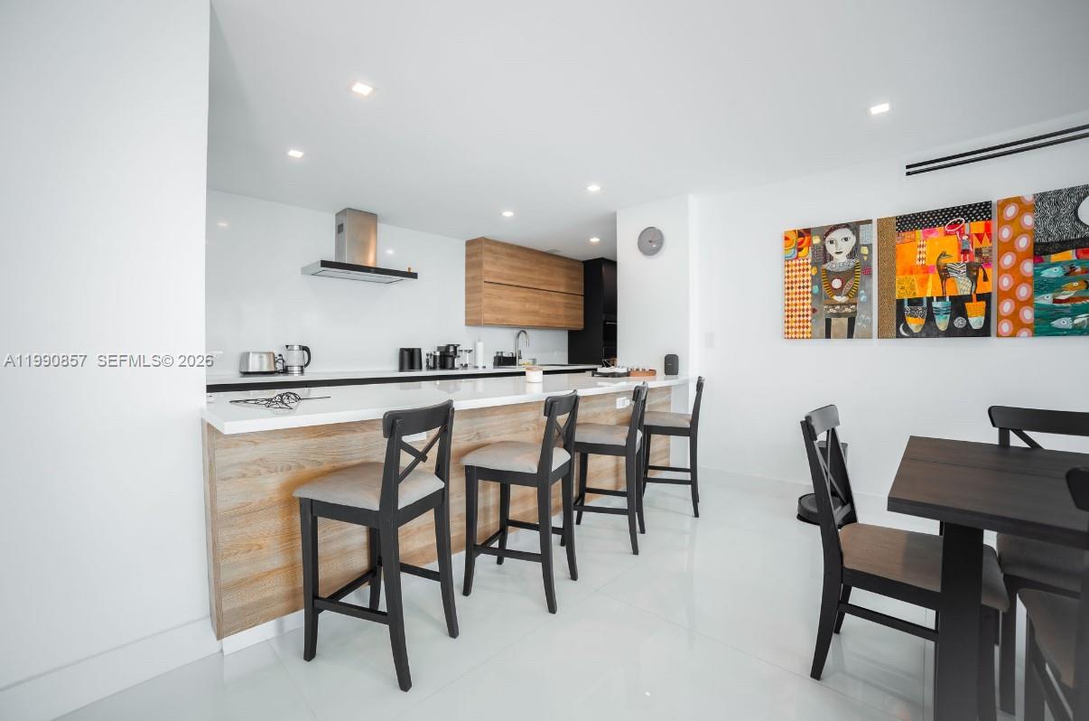 A modern kitchen features a white island with bar stools and colorful wall art — 5600 Collins Ave # 14K, Miami Beach FL 33140, MIAMI BEACH, FL