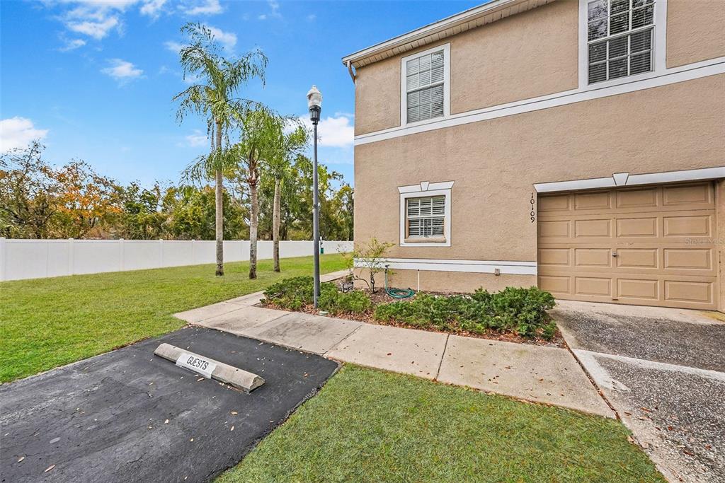 A two-story tan stucco townhouse with a front door and bay window faces a lawn — 10109 BELLEVILLE PLACE, TAMPA, FL