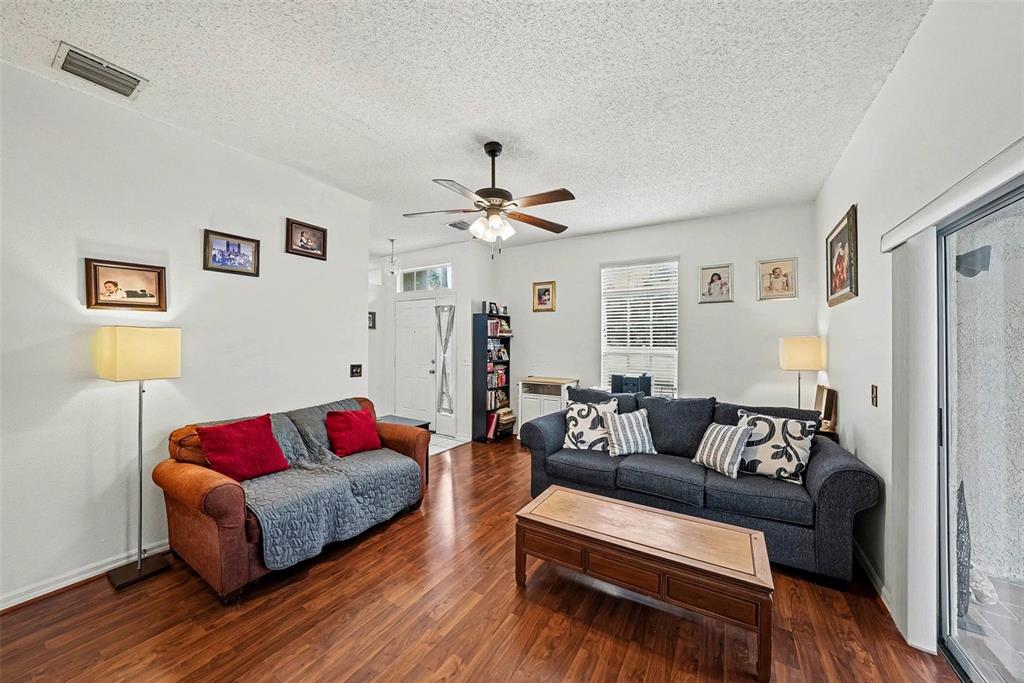 A living room features wood flooring, two sofas, a coffee table, and a ceiling fan — 10109 BELLEVILLE PLACE, TAMPA, FL