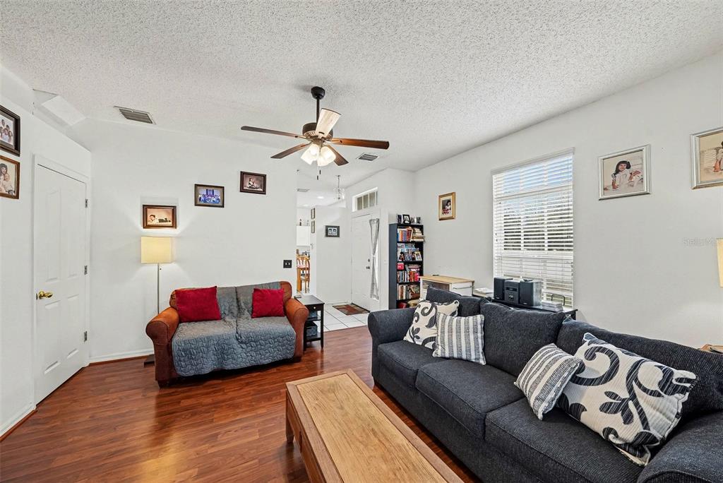 A living room features wood-look flooring, a ceiling fan, and two sofas facing each other — 10109 BELLEVILLE PLACE, TAMPA, FL