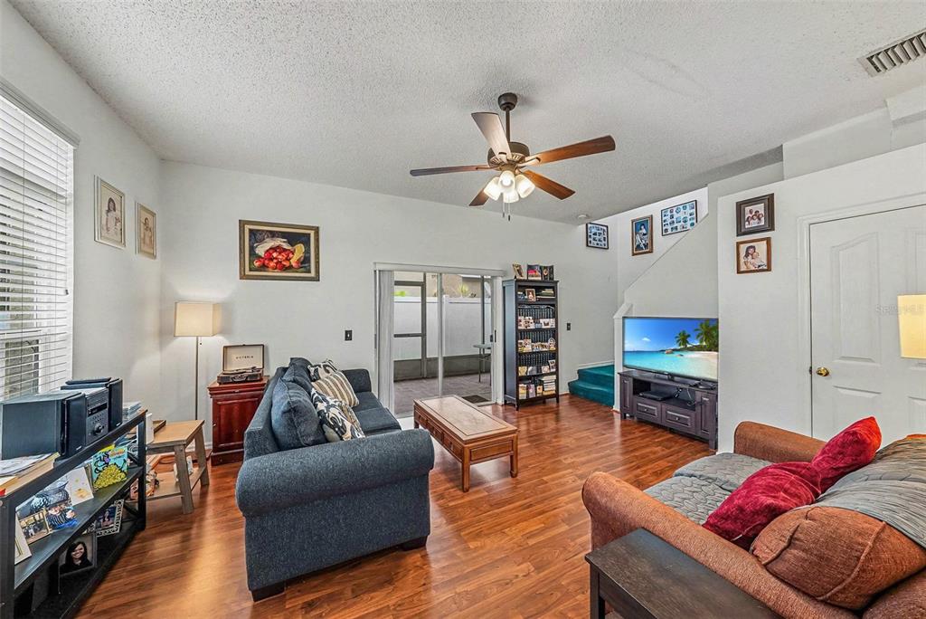 A living room features hardwood floors, a ceiling fan, two sofas, and a sliding glass door — 10109 BELLEVILLE PLACE, TAMPA, FL