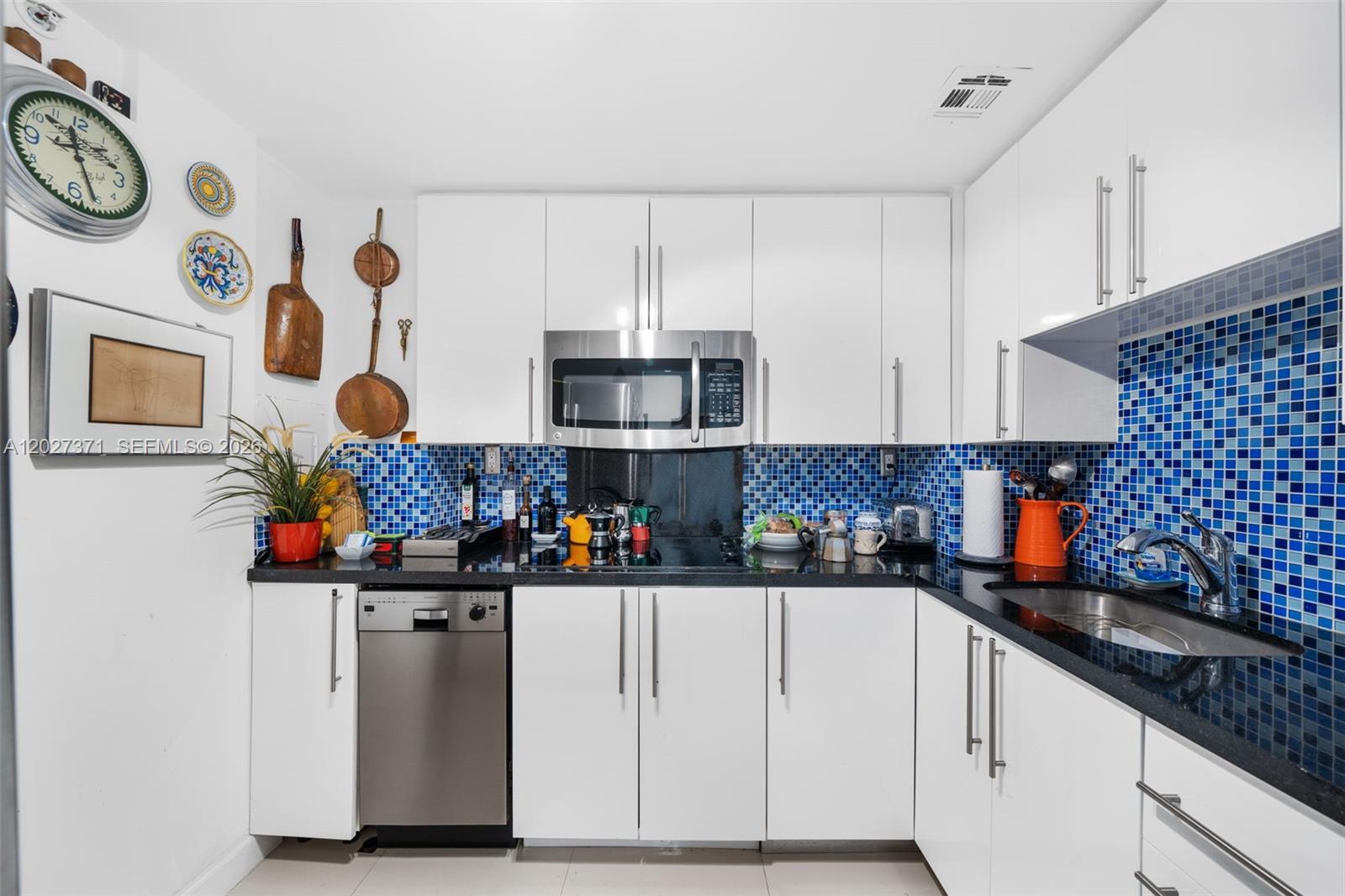 A kitchen features white cabinets, black countertops, and a blue mosaic tile backsplash — 3301 NE 5th Ave # 209, Miami FL 33137, MIAMI, FL