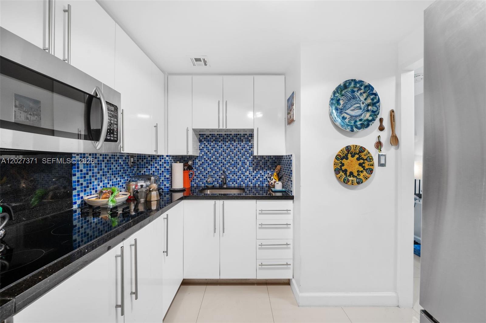 A kitchen features white cabinets, black countertops, and a blue mosaic tile backsplash — 3301 NE 5th Ave # 209, Miami FL 33137, MIAMI, FL