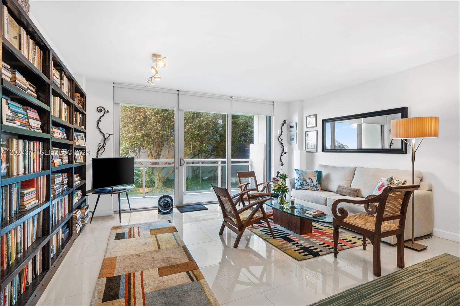 A living room features a large bookshelf, a sofa, two wooden chairs, and a balcony — 3301 NE 5th Ave # 209, Miami FL 33137, MIAMI, FL