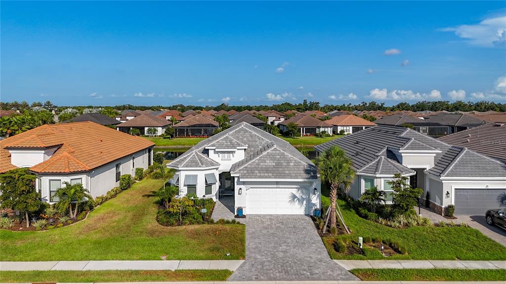 An aerial view shows a suburban house with a gray tiled roof and paver driveway — 6145 GRANDVIEW HILL COURT, BRADENTON, FL