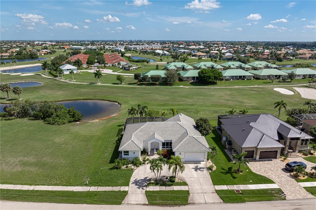 An aerial view shows a single-story house with a pool cage overlooking a golf course — 1612 SUZI STREET, PUNTA GORDA, FL