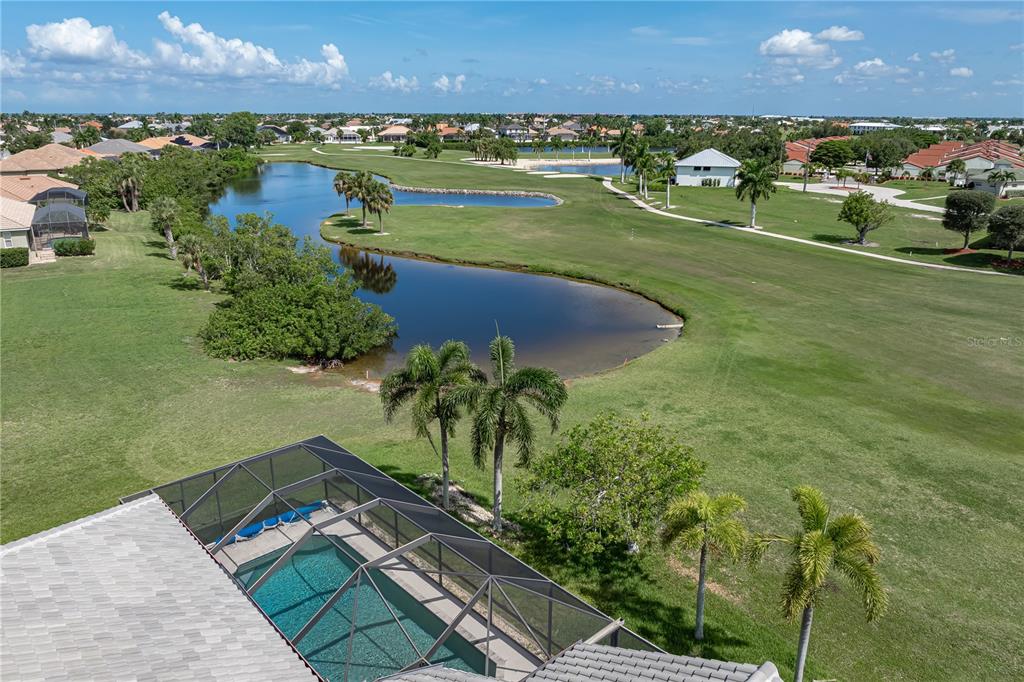 An aerial view shows a screened-in pool behind a house overlooking a golf course pond — 1612 SUZI STREET, PUNTA GORDA, FL