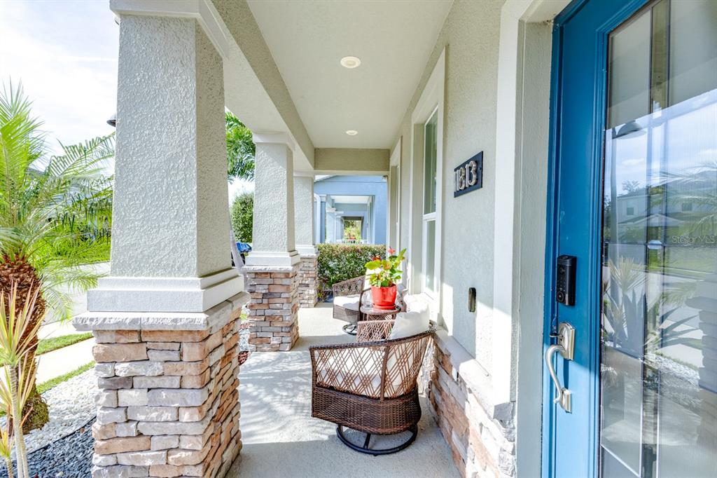A covered front porch features stone-based columns, wicker chairs, and a bright blue front door — 11813 GINSBERG PLACE, ORLANDO, FL