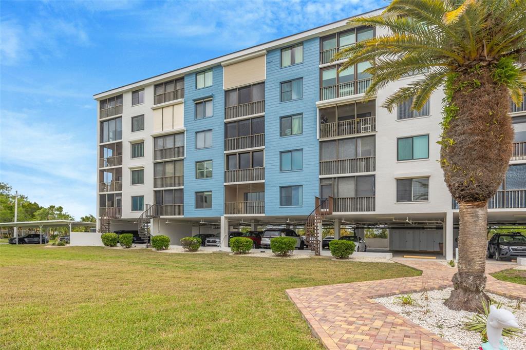 A multi-story apartment building with covered parking on the ground level and a palm tree — 4620 BAY BOULEVARD UNIT 1117, PORT RICHEY, FL