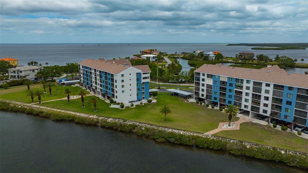An aerial view shows two multi-story apartment buildings situated on a grassy waterfront lot — 4620 BAY BOULEVARD UNIT 1117, PORT RICHEY, FL