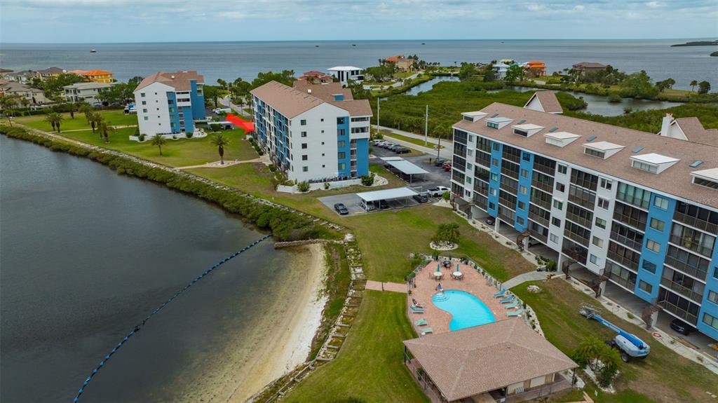 An aerial view shows two large waterfront apartment buildings with a pool and parking area — 4620 BAY BOULEVARD UNIT 1117, PORT RICHEY, FL
